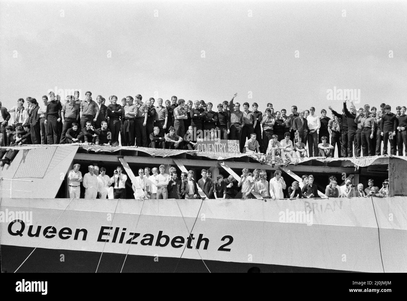 Il QE2 torna a casa a Southampton. Union Jacks è festooned sulle automobili, drappeggiato sulle spalle, ondulato sui bastoni. Southampton dà il benvenuto a "Three Cheers" al QE2 lussuoso liner trasformato in trooper di ritorno dalla guerra. A bordo è il suo prezioso carico, i 700 sopravvissuti della HMS Coventry, ardent e Antelope, affondati nella battaglia per le Falklands. 11th giugno 1982. Foto Stock