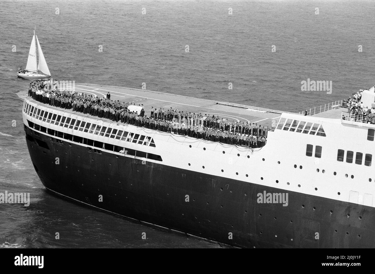 Il QE2 torna a casa a Southampton. Union Jacks è festooned sulle automobili, drappeggiato sulle spalle, ondulato sui bastoni. Southampton dà il benvenuto a "Three Cheers" al QE2 lussuoso liner trasformato in trooper di ritorno dalla guerra. A bordo è il suo prezioso carico, i 700 sopravvissuti della HMS Coventry, ardent e Antelope, affondati nella battaglia per le Falklands. 11th giugno 1982. Foto Stock