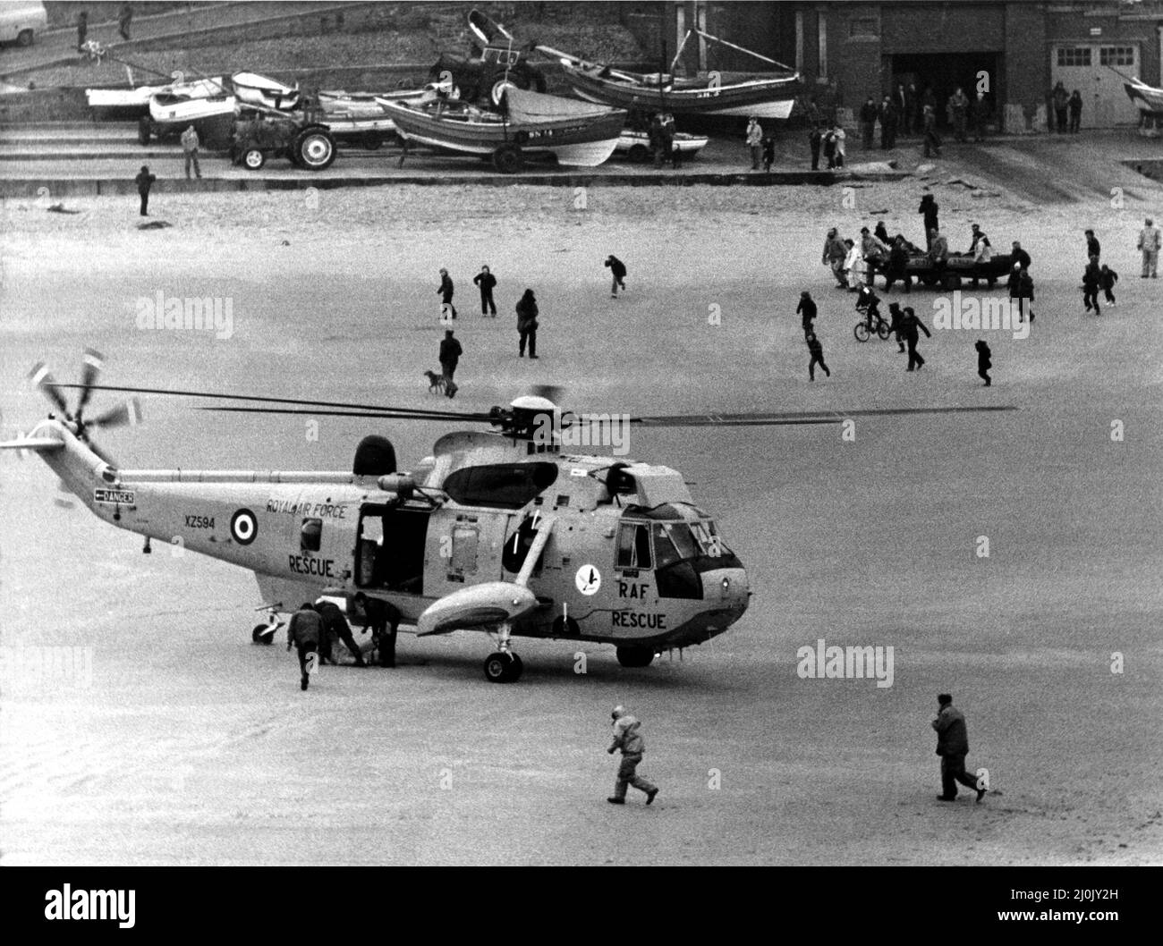 Una ricerca e salvataggio RAF Sea King da RAF Boulmer atterra un uomo sulla spiaggia dopo che è stato strappato fuori dal mare al largo di Cullercoats. Sullo sfondo si trova la nave di salvataggio costiera che si era ribaltata viene tirata a terra. L'elicottero era stato coinvolto nel doppio salvataggio in venti alti che aveva iniziato con una barca da pesca capsizing seguito dalla barca di salvataggio facendo lo stesso. Due uomini sono stati salvati dal re del Mare, un altro uomo è riuscito a nuotare di nuovo alla riva whist un quarto annegato intrappolato da alghe e corda dalla barca. 22/02/1981. Foto Stock