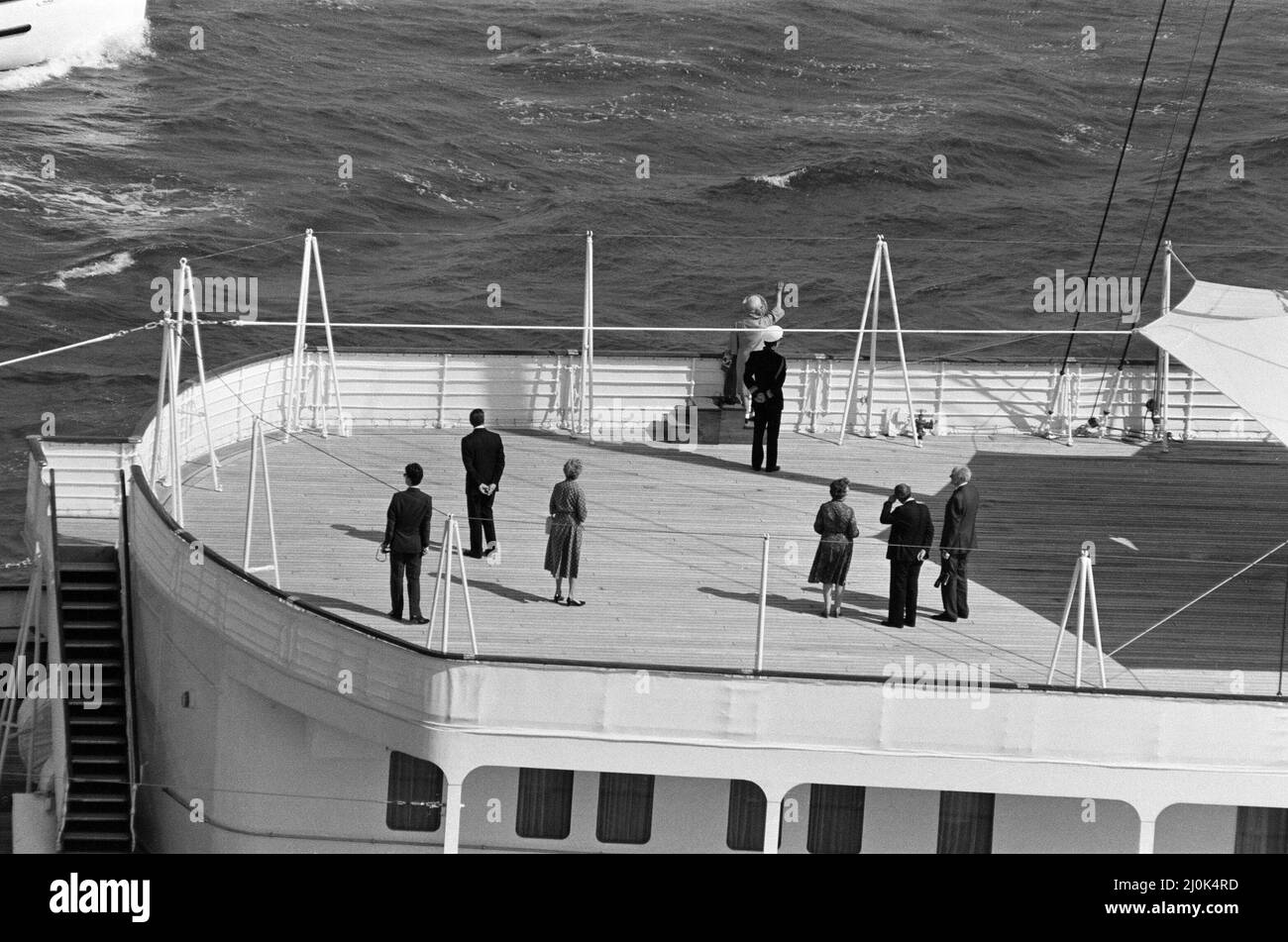 Il QE2 torna a casa a Southampton. Union Jacks è festooned sulle automobili, drappeggiato sulle spalle, ondulato sui bastoni. Southampton dà il benvenuto a "Three Cheers" al QE2 lussuoso liner trasformato in trooper di ritorno dalla guerra. A bordo è il suo prezioso carico, i 700 sopravvissuti della HMS Coventry, ardent e Antelope, affondati nella battaglia per le Falklands. Nella foto, l'incontro del QE2 con Royal Yacht Britannia, la Regina Madre che ondeggiava dal ponte di poppa. 11th giugno 1982. Foto Stock