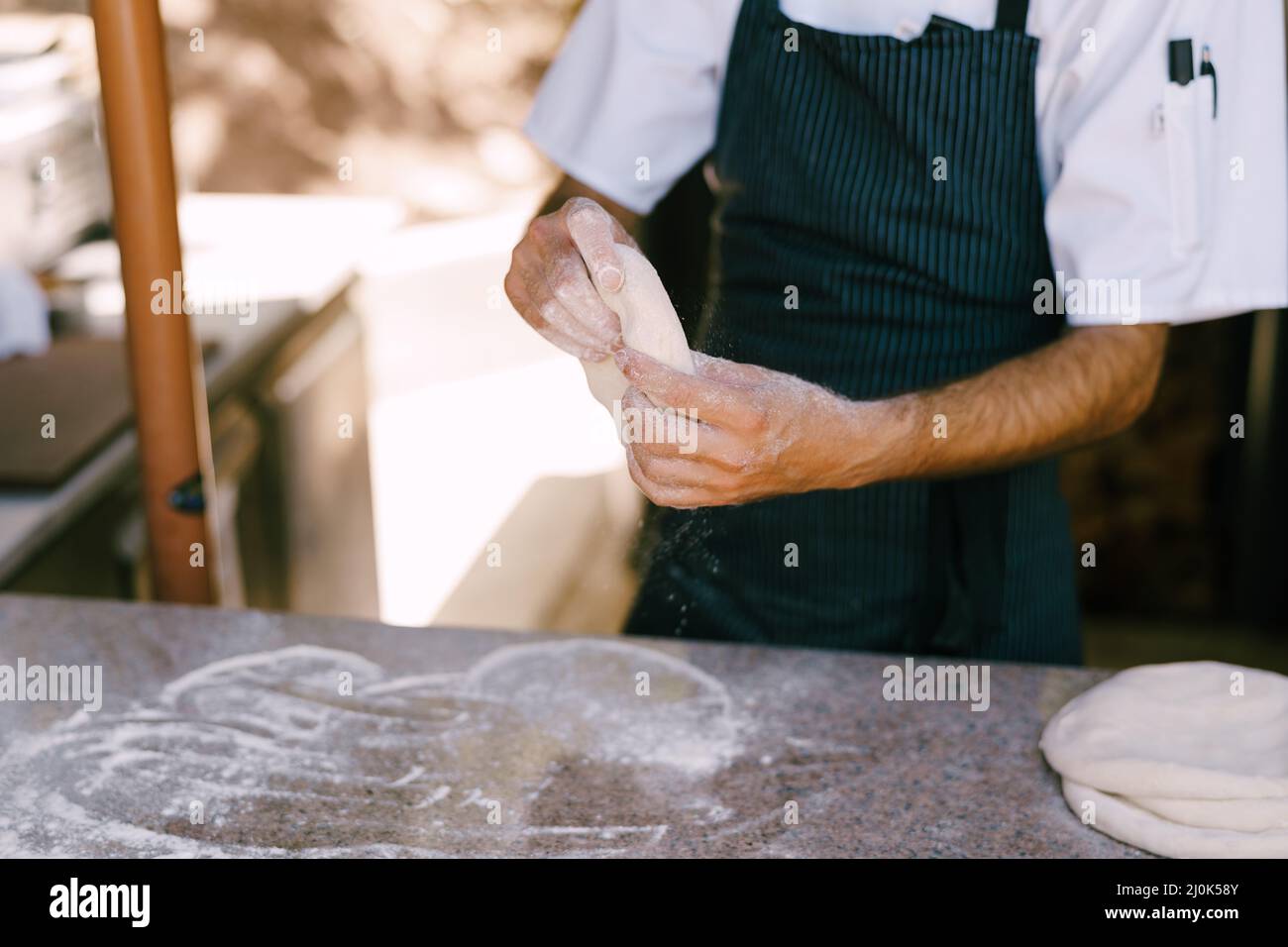 Primo piano delle mani dello chef. Prepara l'impasto per la pizza, arrotola con le mani in forme rotonde. Foto Stock