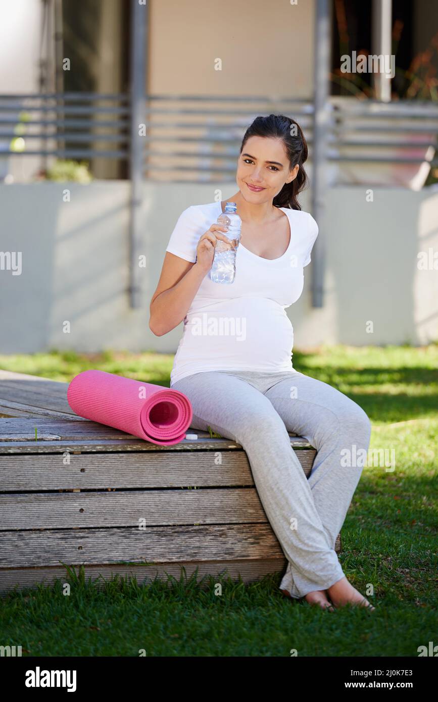Dopo un allenamento di yoga, ti sentirai ristorato. Shot di una giovane donna incinta seduta con il suo tappeto yoga all'esterno. Foto Stock
