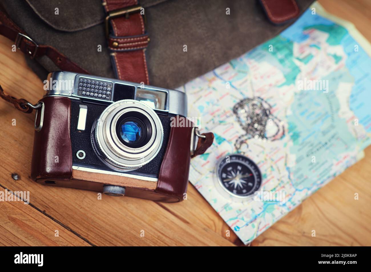 Non smettere mai di esplorare. Scatto di una macchina fotografica, mappa, bussola e borsa su un tavolo di legno. Foto Stock