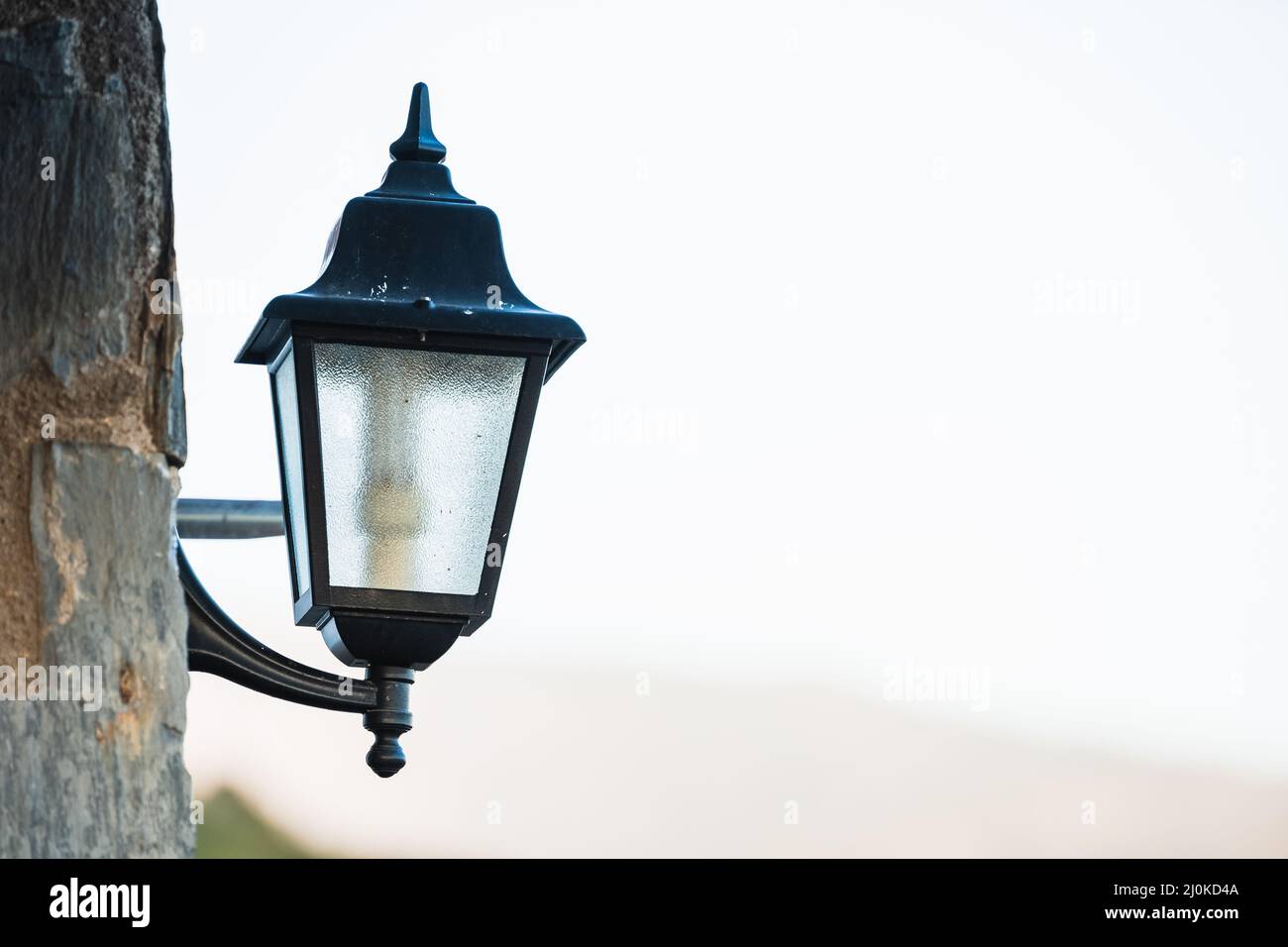 Scatto verticale di una lanterna di strada nera appesa su un palo di legno contro il cielo luminoso durante il giorno Foto Stock