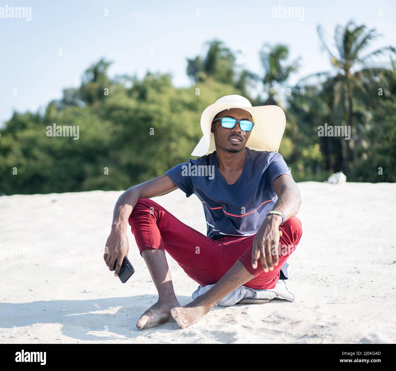 Uomo africano seduto solo sulla spiaggia sabbiosa Foto Stock