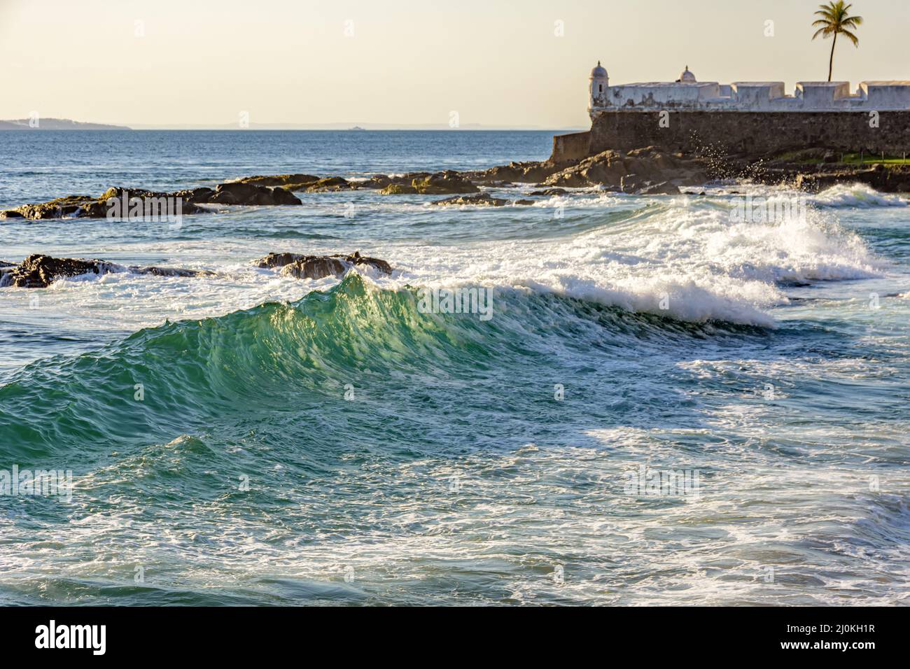 Salvador onde di mare con vecchia fortezza coloniale sullo sfondo Foto Stock
