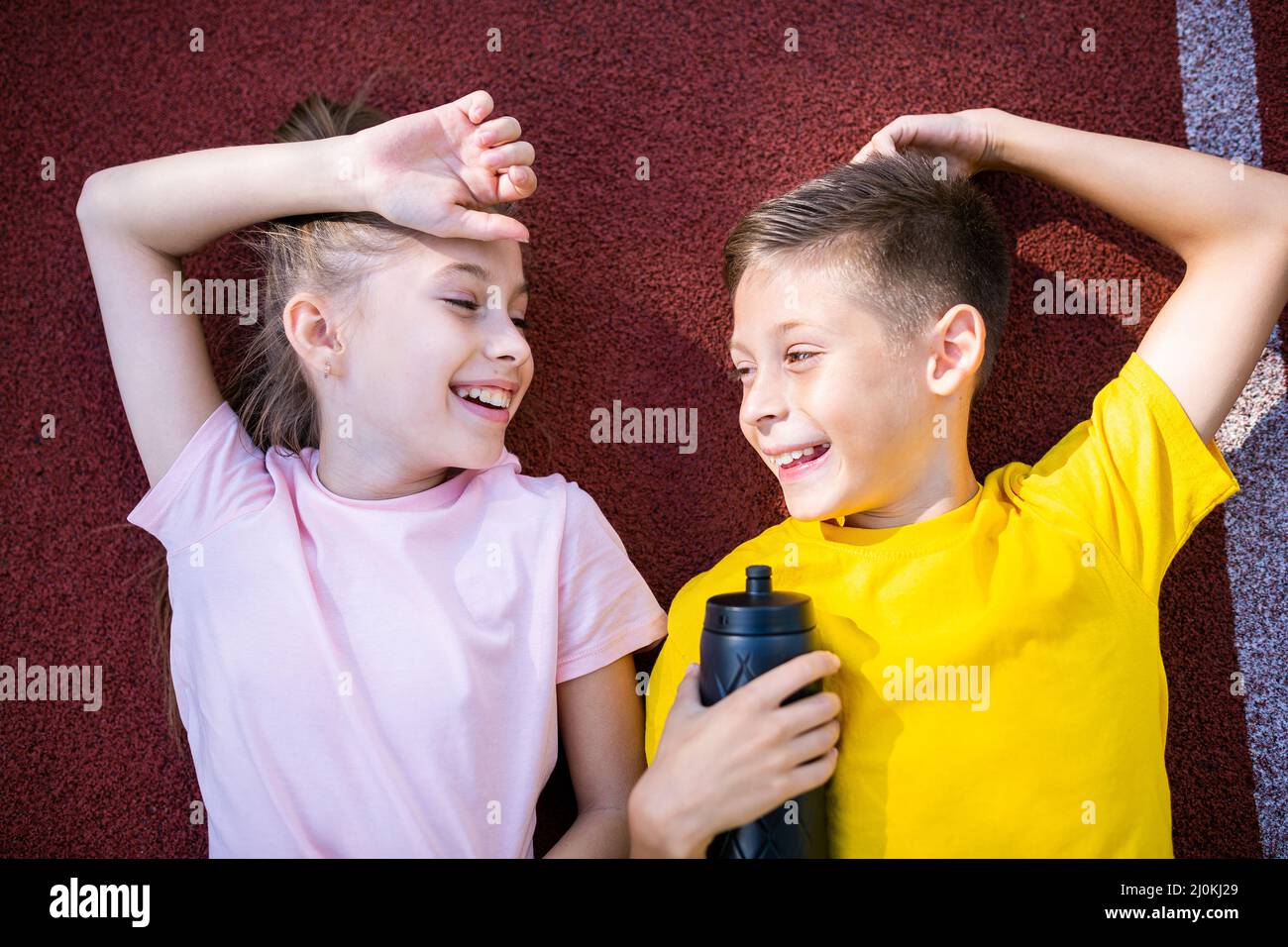 Due bambini felici, ragazzo e una ragazza, si stendono sulle spalle e  ridono guardando la macchina fotografica dopo aver fatto jogging allo stadio  runnin Foto stock - Alamy