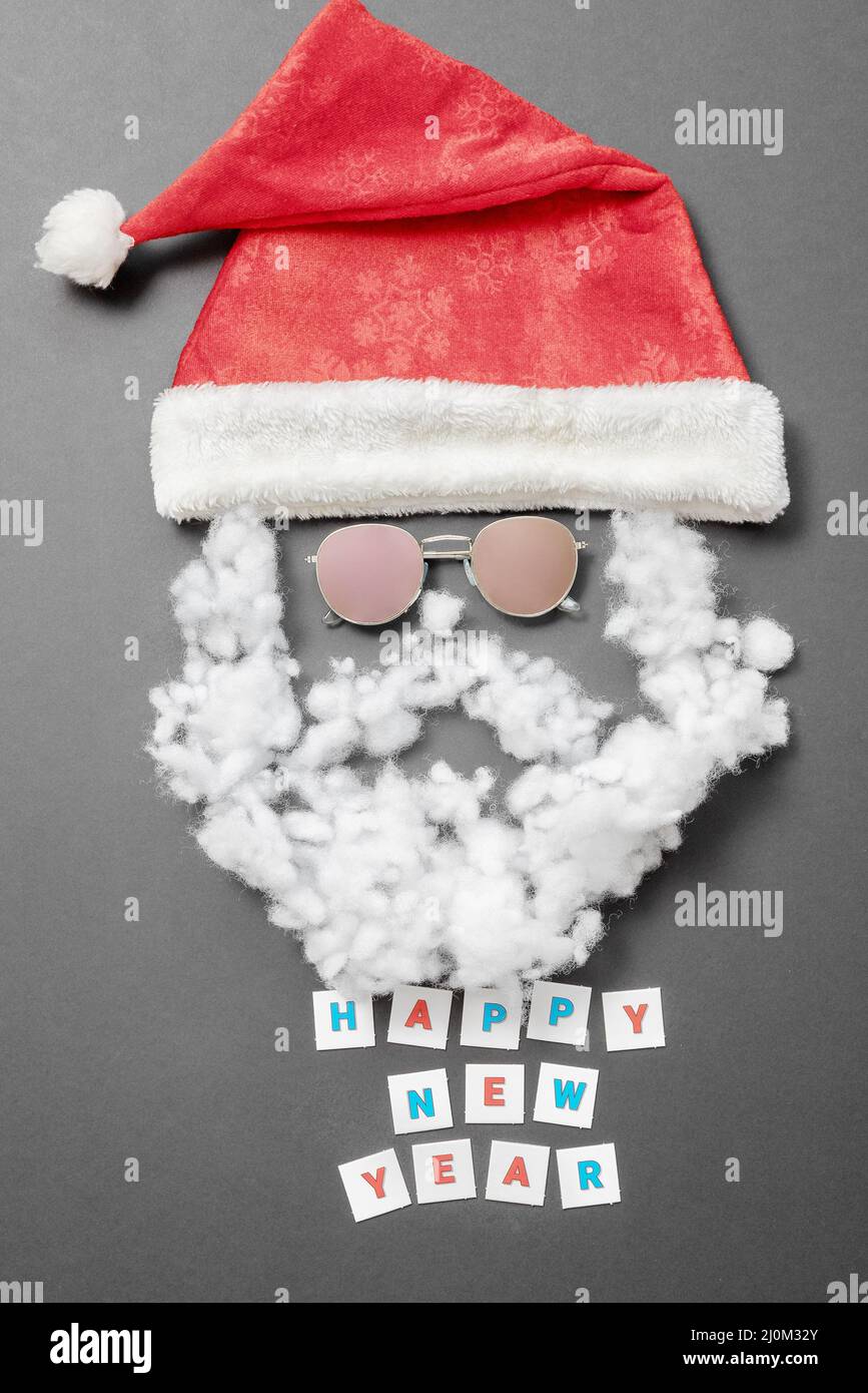 Cappello Santa in velluto con baffi da occhiali da sole con barba e l'iscrizione Felice anno nuovo su sfondo grigio. Tessera di Capodanno Foto Stock