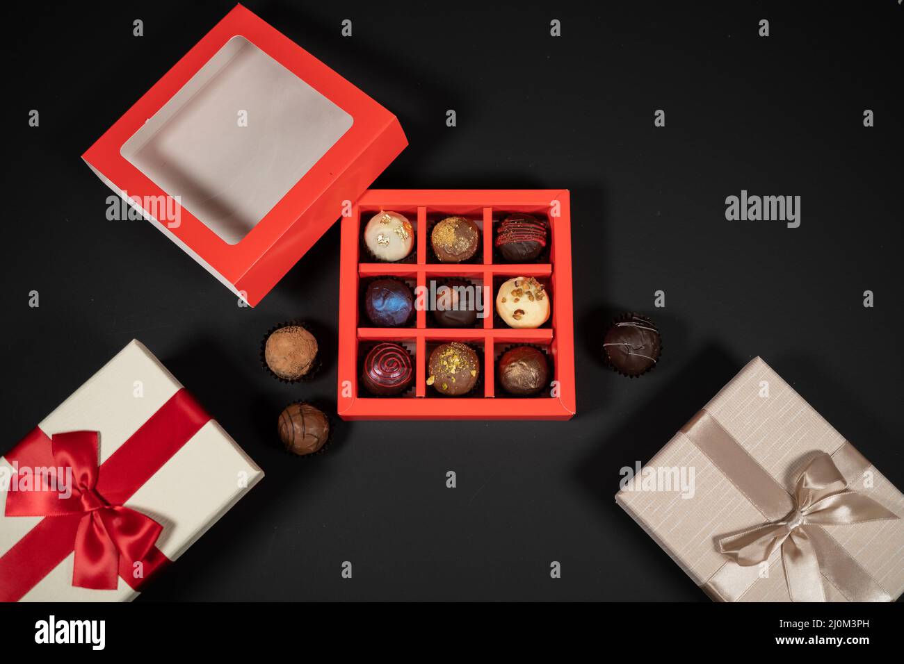 Varie caramelle al tartufo di cioccolato fatte a mano in una scatola rossa su sfondo scuro. Direttamente sopra la vista dall'alto. Foto Stock