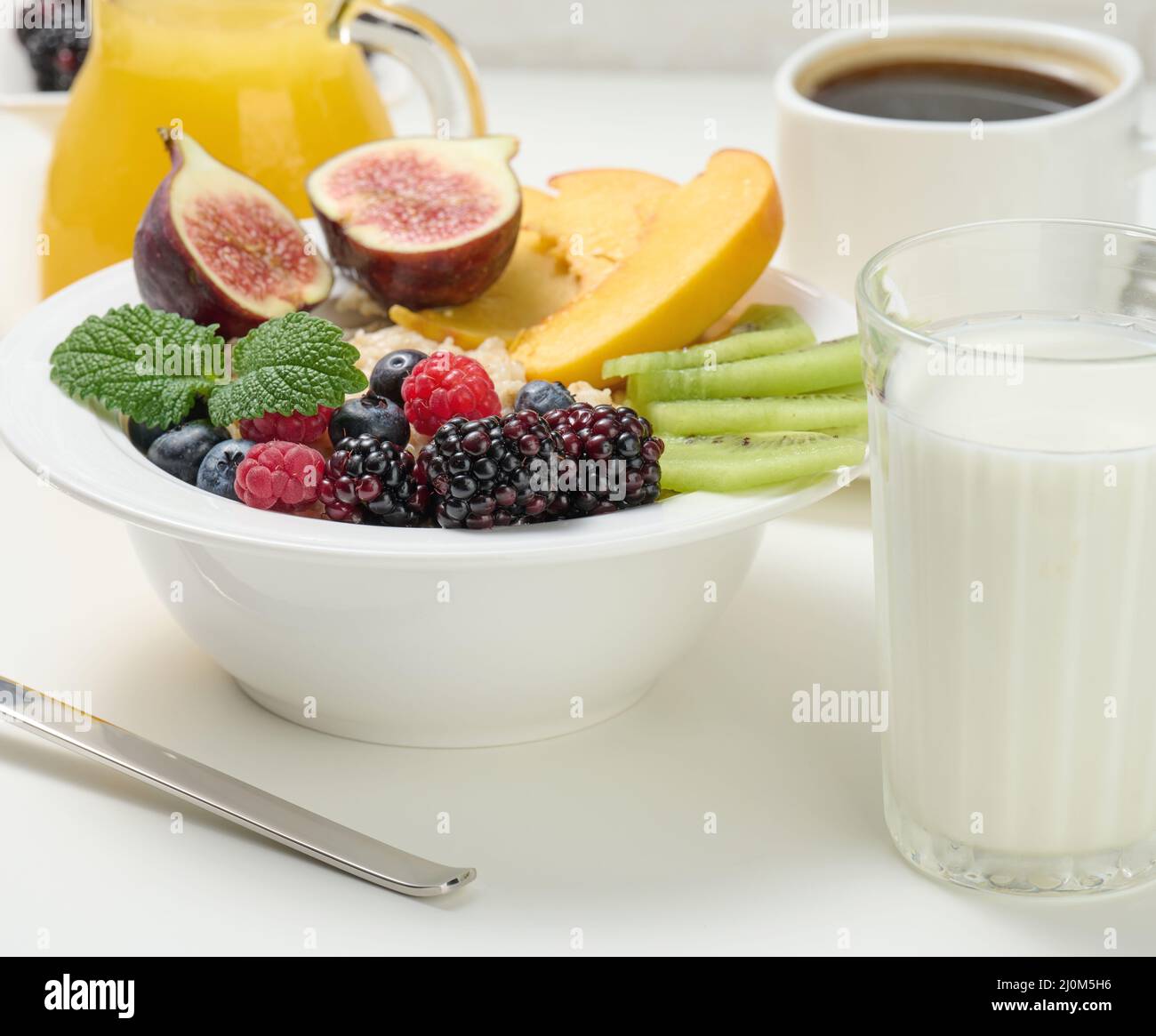 Piatto completo con farinata d'avena e frutta, succo appena spremuto in un decanter trasparente in vetro, tazza di caffè su un tavolo bianco. Healt Foto Stock