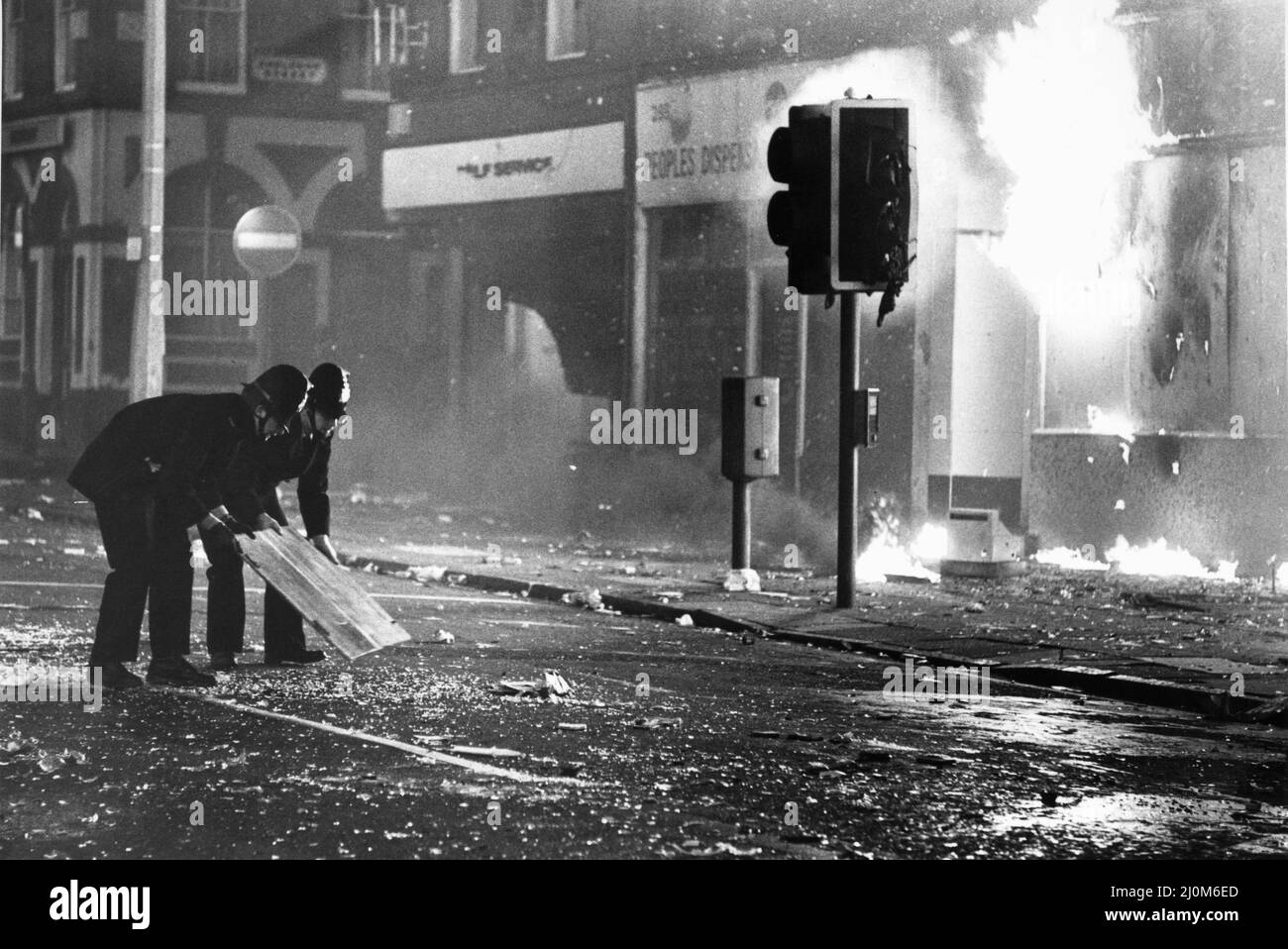 Toxteth Riot 6th luglio 1981Police gli ufficiali cercano di eliminare il vetro rotto da Park Road fuori da un negozio di saccheggio in fiamme, in modo che i vigili del fuoco possano controllare il fuoco. Le rivolte sono state innescate a seguito dell'intercettazione da parte della polizia dei motociclisti Leroy Cooper in Selbourne Street. Una folla si riunì, la chiamata di nome crebbe in pochi minuti ci fu un fraas su vasta scala che vide tre poliziotti feriti e un giovane uomo locale, arrestato con accuse d'assalto. Non si è fermata qui. La polizia ha montato pattuglie extra nella zona e all'inizio della sera successiva, 4 luglio, sono stati sotto attacco da una folla armata Foto Stock