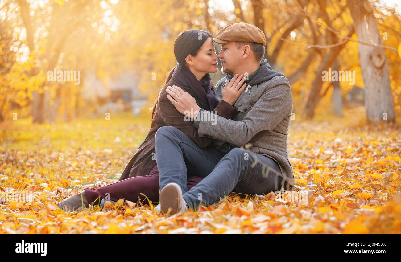 Coppia romantica seduta su Fall Foliage naso a naso con occhi chiusi nel sobborgo d'autunno. L'uomo bello abbraccia la sua amata Donna. Casual Foto Stock