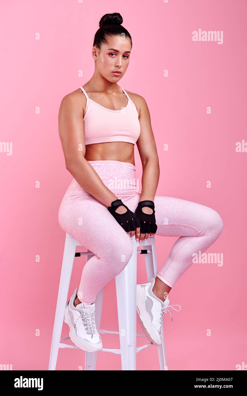 Shes una donna dura. Ritratto da studio di una giovane donna sportiva seduta su una sedia su sfondo rosa. Foto Stock