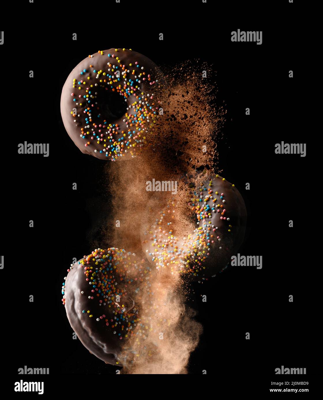 Ciambelle rotonde al cioccolato con zucchero multicolore cosparge di levitate in una nuvola di cacao marrone su sfondo nero Foto Stock