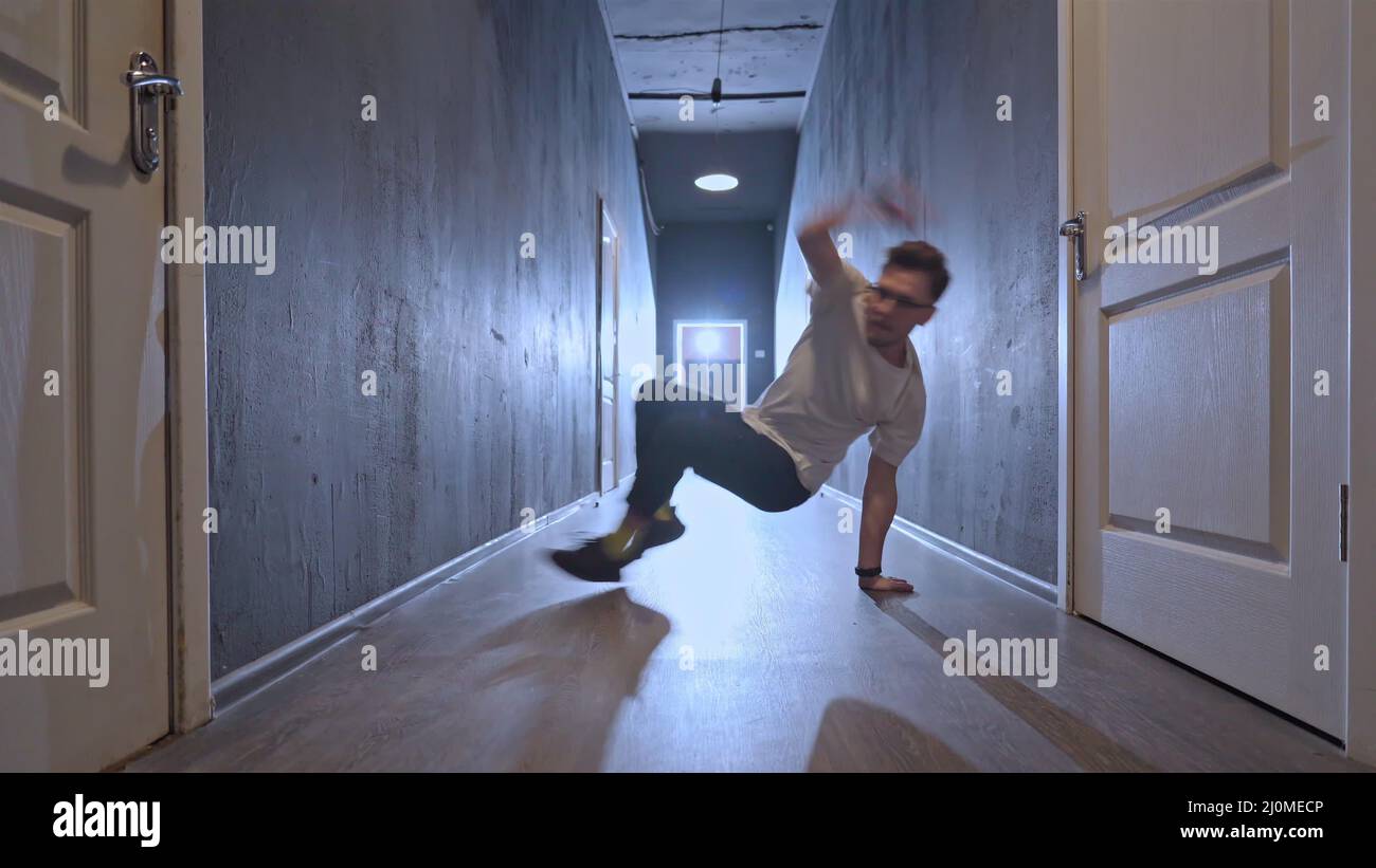 Ballerino contemporaneo hip hop giovane che balla in un raggio di luce in un lungo corridoio scuro con molte porte bianche su entrambi i lati. 4 Foto Stock