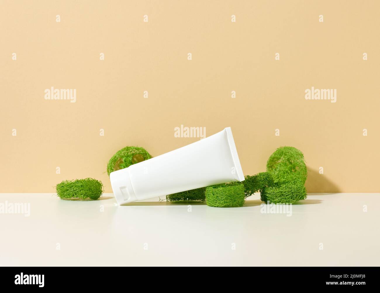 Tubo di plastica bianco vuoto su sfondo beige e pezzi di loofah verde. Prodotti cosmetici per marcare a caldo gel, crema, lozione, cenere Foto Stock