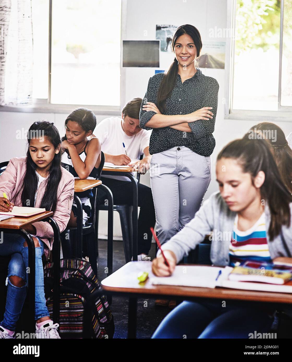 Potete fidarvi di me con la vostra educazione dei bambini. Ritratto di una giovane insegnante attraente in piedi con le braccia ripiegate in una classe. Foto Stock