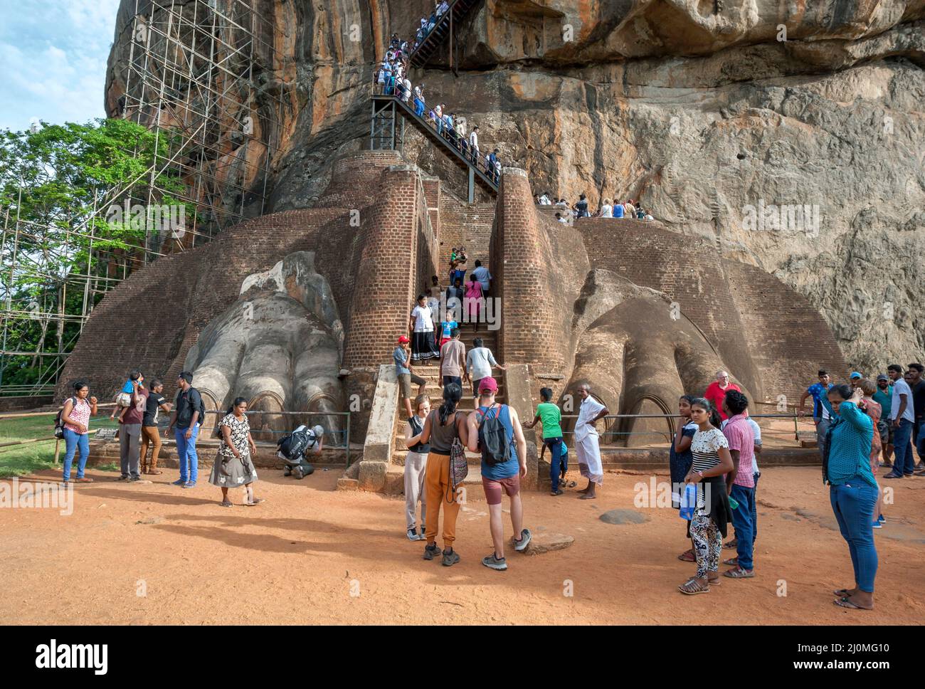 I turisti si trovano accanto ai Lions Paws sulla piattaforma Lion presso la fortezza rocciosa di Sigiriya in Sri Lanka. Sullo sfondo c'è la scalinata che porta alla cima Foto Stock