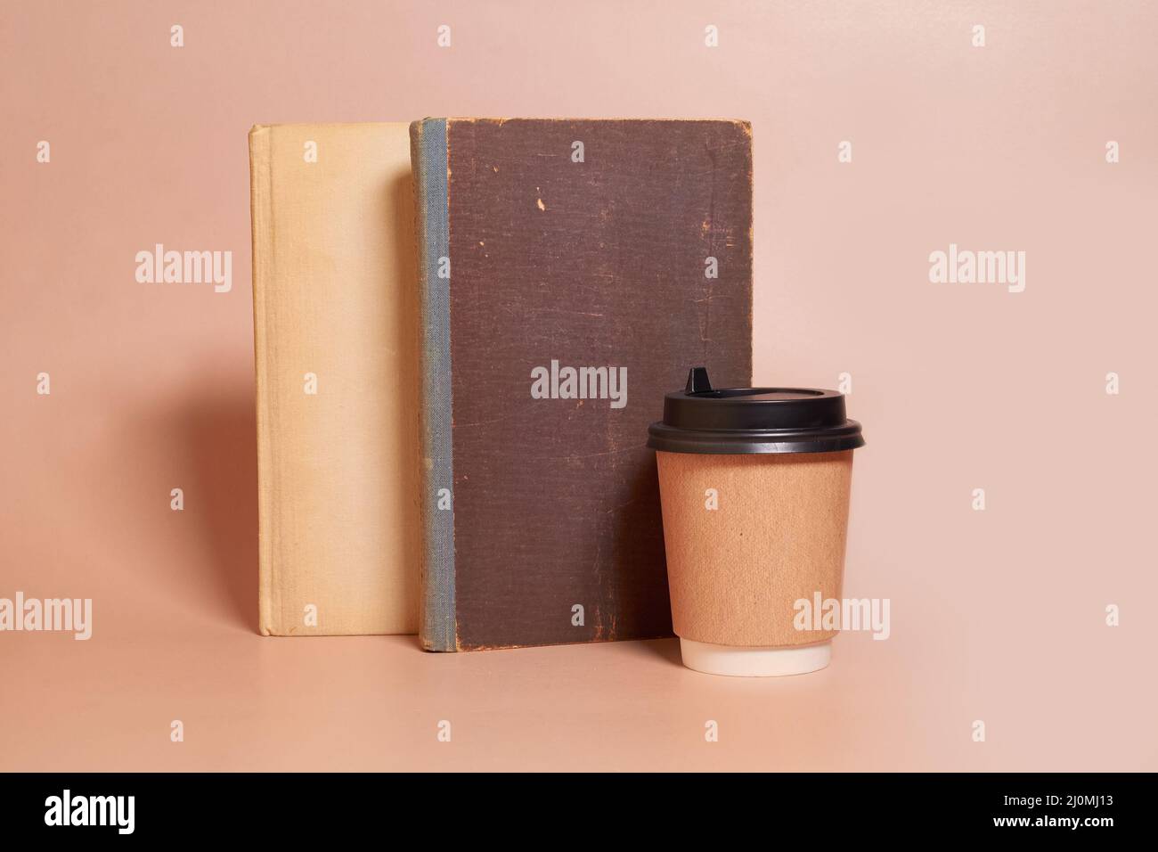 Beffa. Una tazza di carta di caffè si trova accanto a una pila di vecchi libri Foto Stock