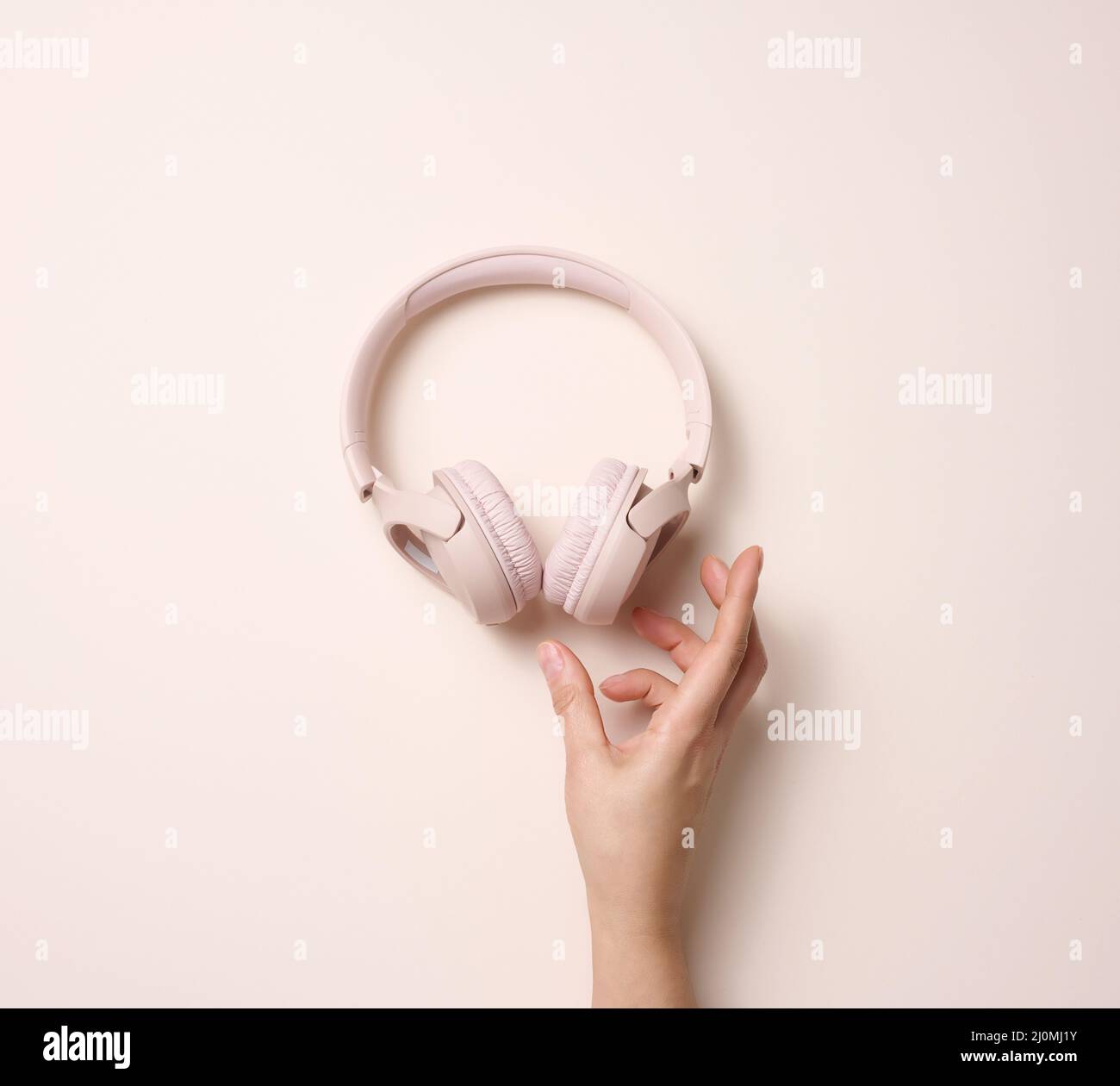 Cuffie wireless rosa femmina con tenuta a mano su sfondo beige, vista dall'alto Foto Stock