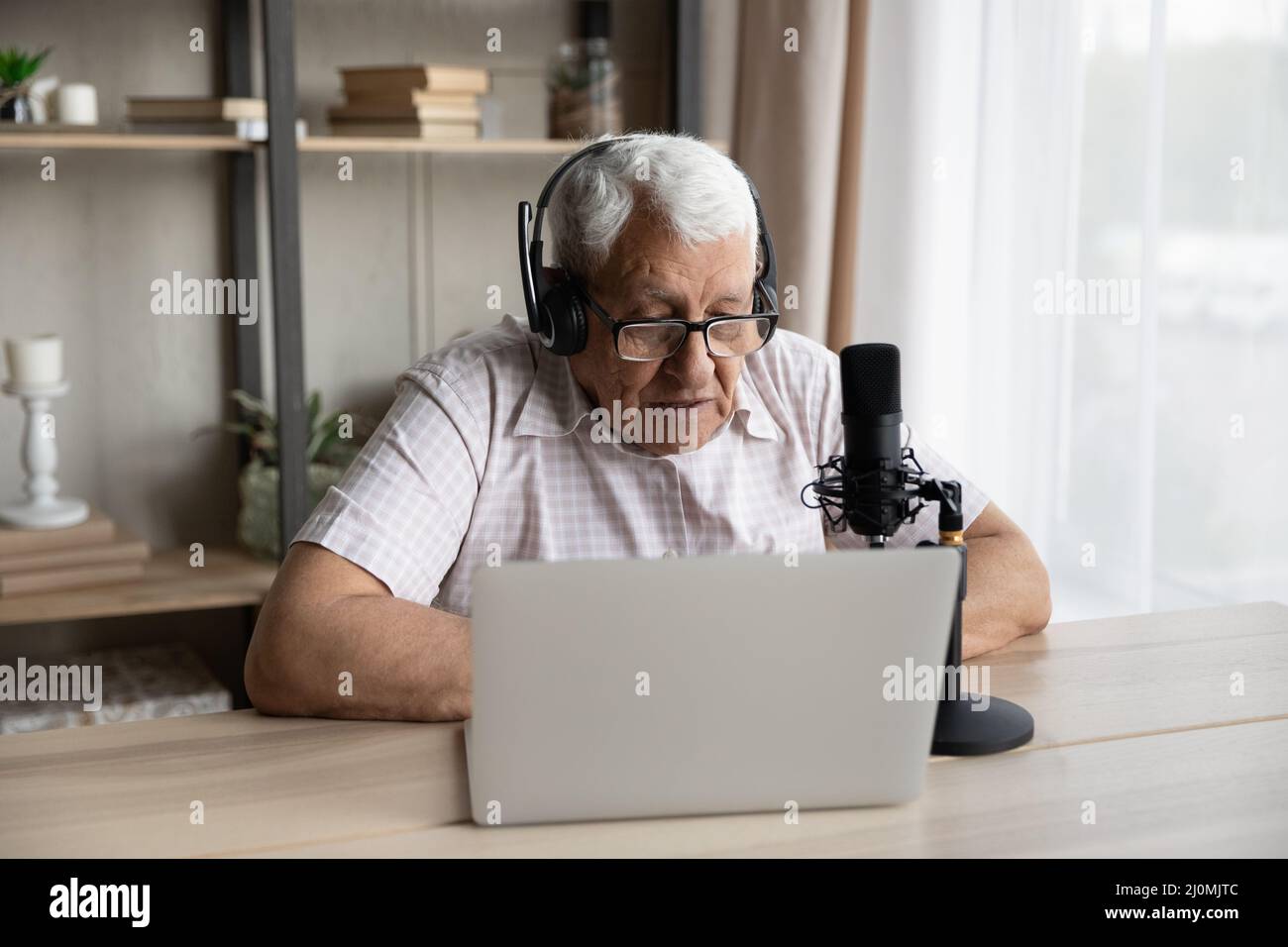 L'uomo anziano indossa le cuffie e guarda il laptop che parla nel microfono Foto Stock
