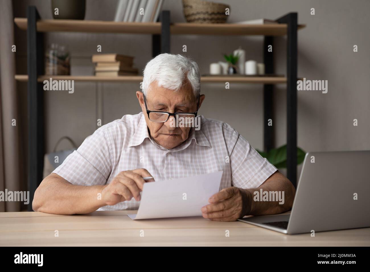Uomo più anziano serio indossare occhiali leggere documento seduto al tavolo Foto Stock