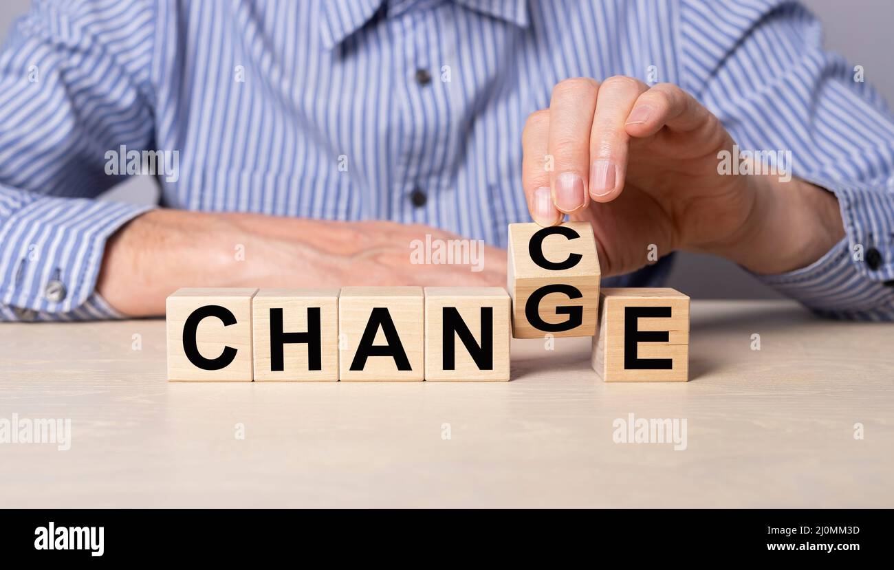 Cubo di ribaltamento a mano con possibilità di cambiamento di parola. Uomo seduto a tavola con cubetti di legno. Sviluppo personale, crescita professionale, successo, concetto di pensiero positivo. Foto di alta qualità Foto Stock