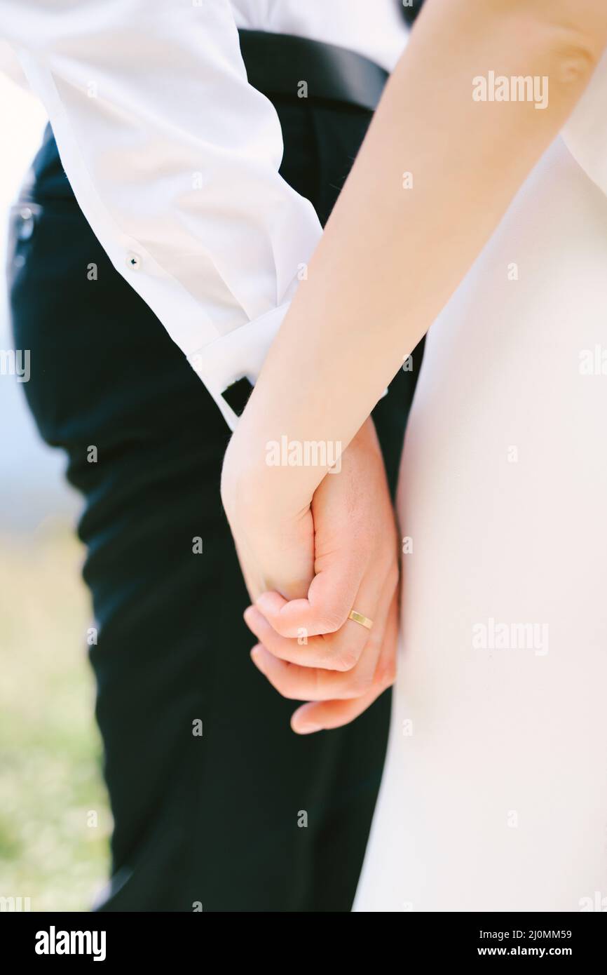 Mano dello sposo in una camicia bianca e pantaloni neri tiene la mano della sposa in un abito bianco. Primo piano Foto Stock