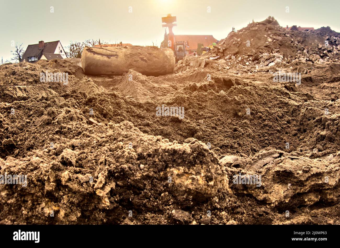 Vista dal suolo sul sottogrado sabbioso di un cantiere con un serbatoio di terra scavato e un escavatore sullo sfondo Foto Stock