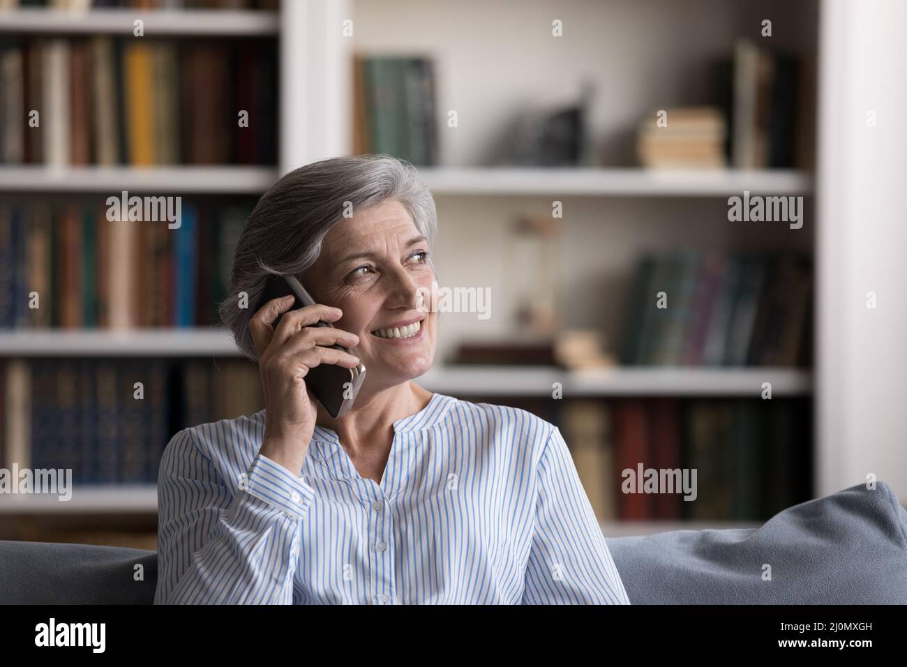 La donna più anziana si siede sul divano parlando con un amico sullo smartphone Foto Stock