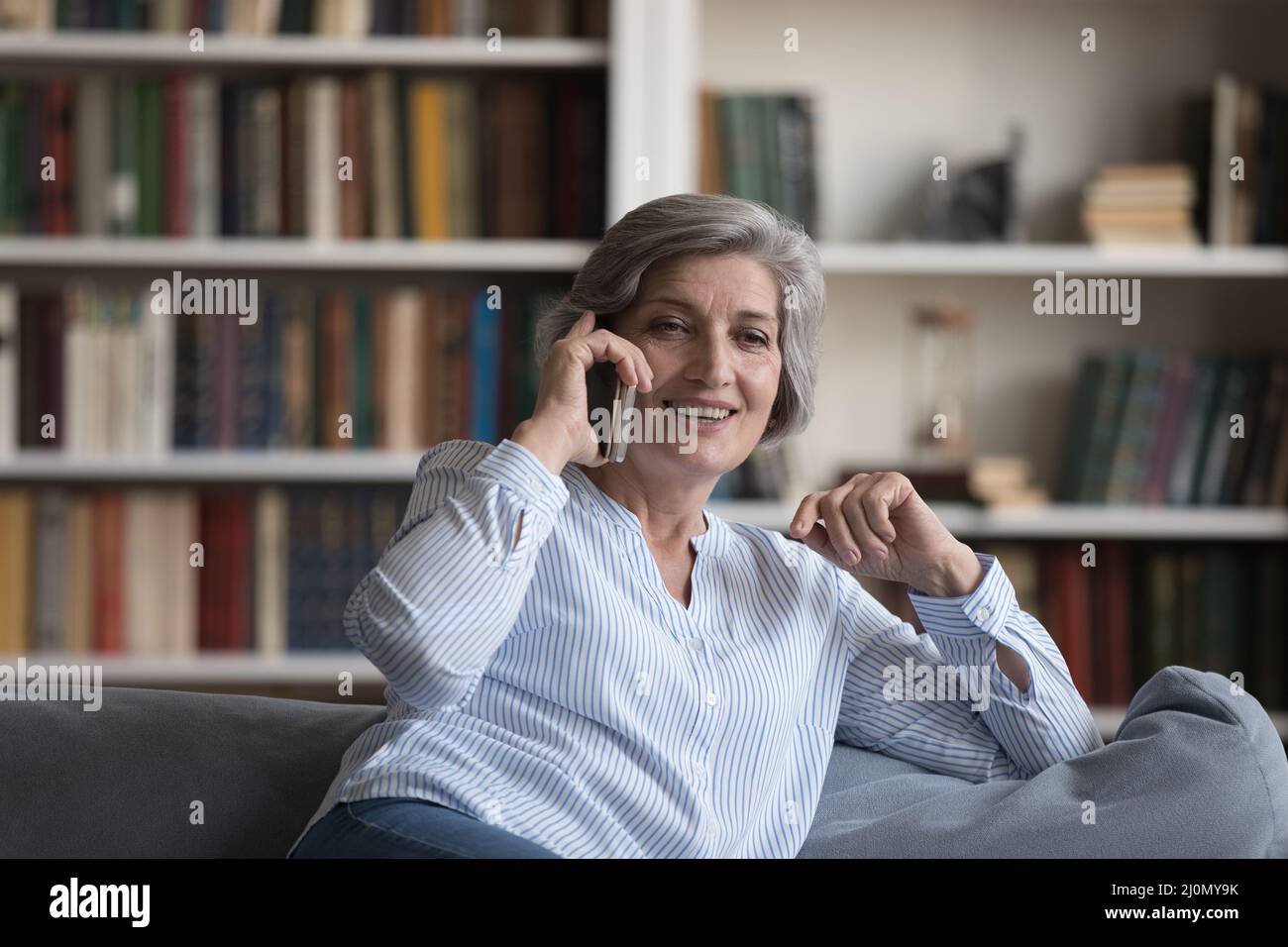 Donna più anziana che si rilassa sul divano tiene il cellulare che ha piacevole conversazione Foto Stock