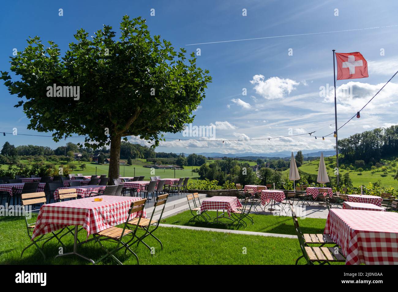 Idilliaco ristorante all'aperto con una splendida vista e tavoli colorati in una terrazza erbosa sul cortile delle Alpi svizzere Foto Stock