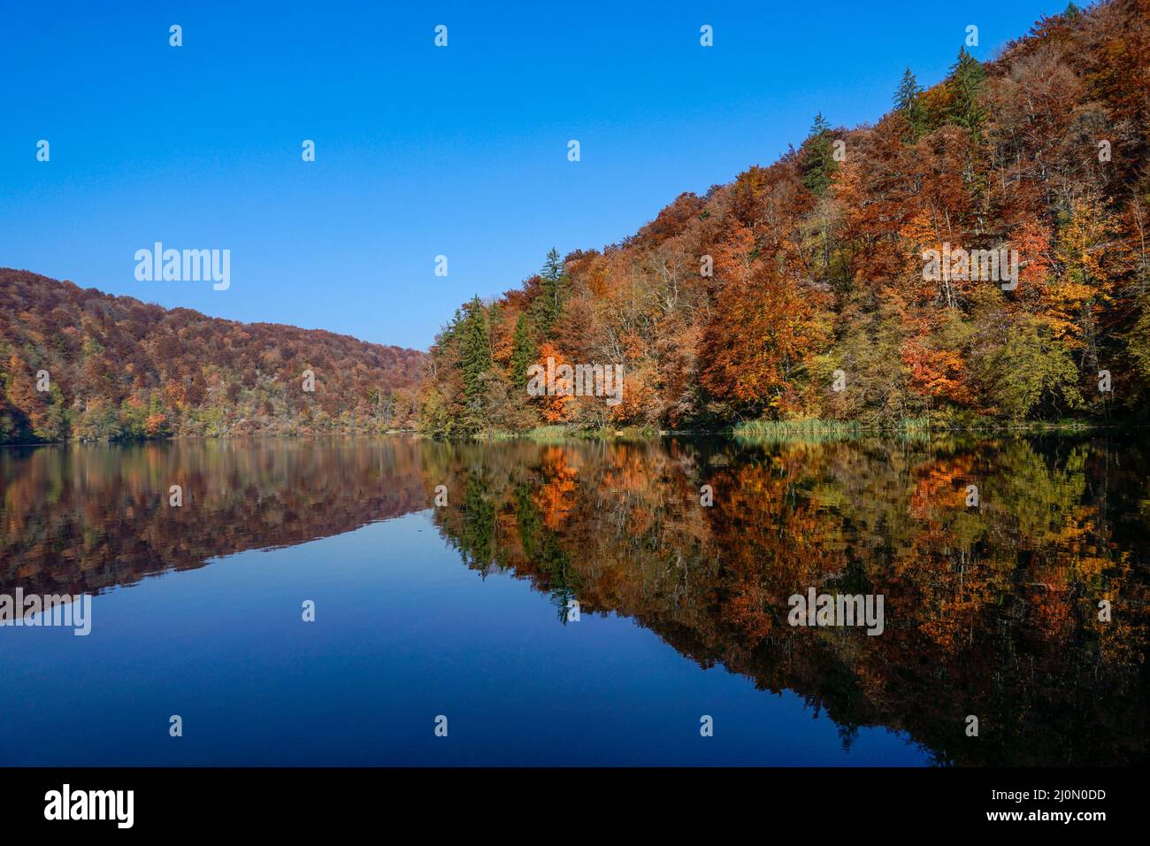Lago blu calmo con riflessi di colline e foreste in intensi colori autunnali Foto Stock