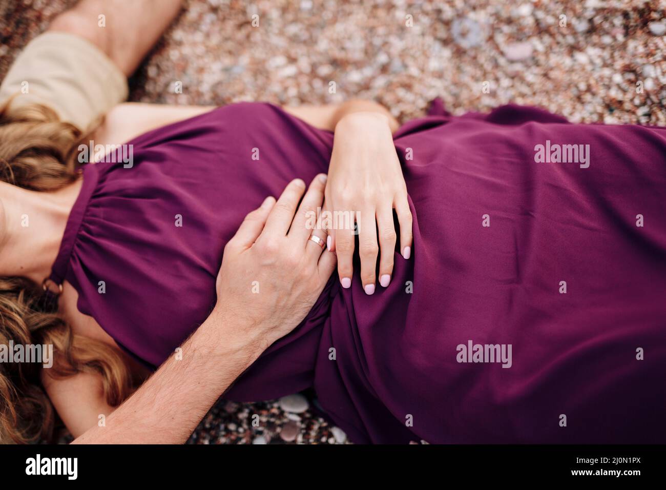 Sposa in un abito borgogna si trova su un ciottolo con le mani piegate sul suo stomaco. Primo piano Foto Stock