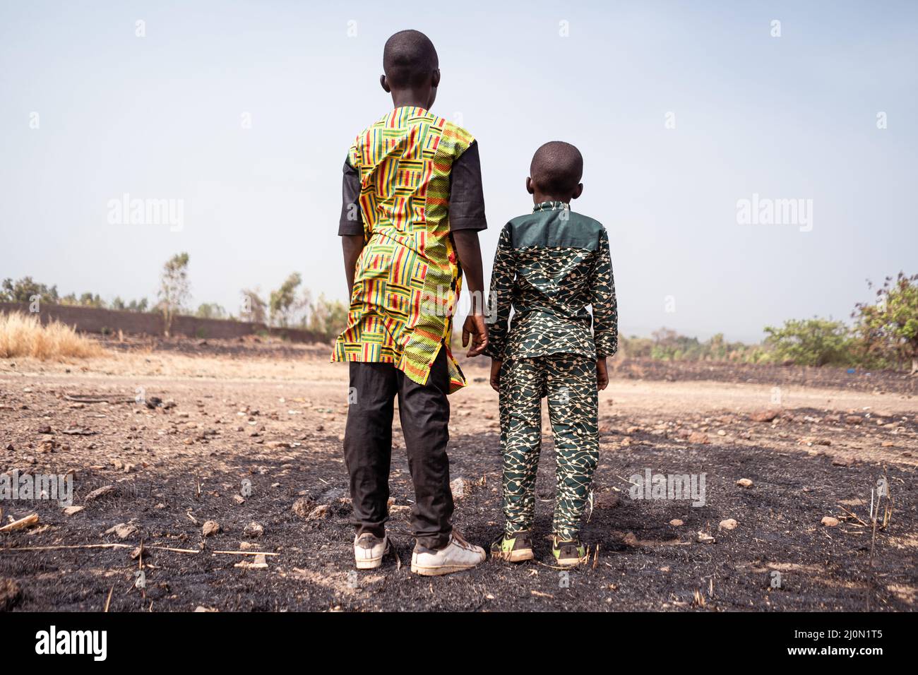 Due bambini africani si trovano disperatamente di fronte a un campo di grano bruciato.crisi climatica, simbolo del riscaldamento globale. Foto Stock