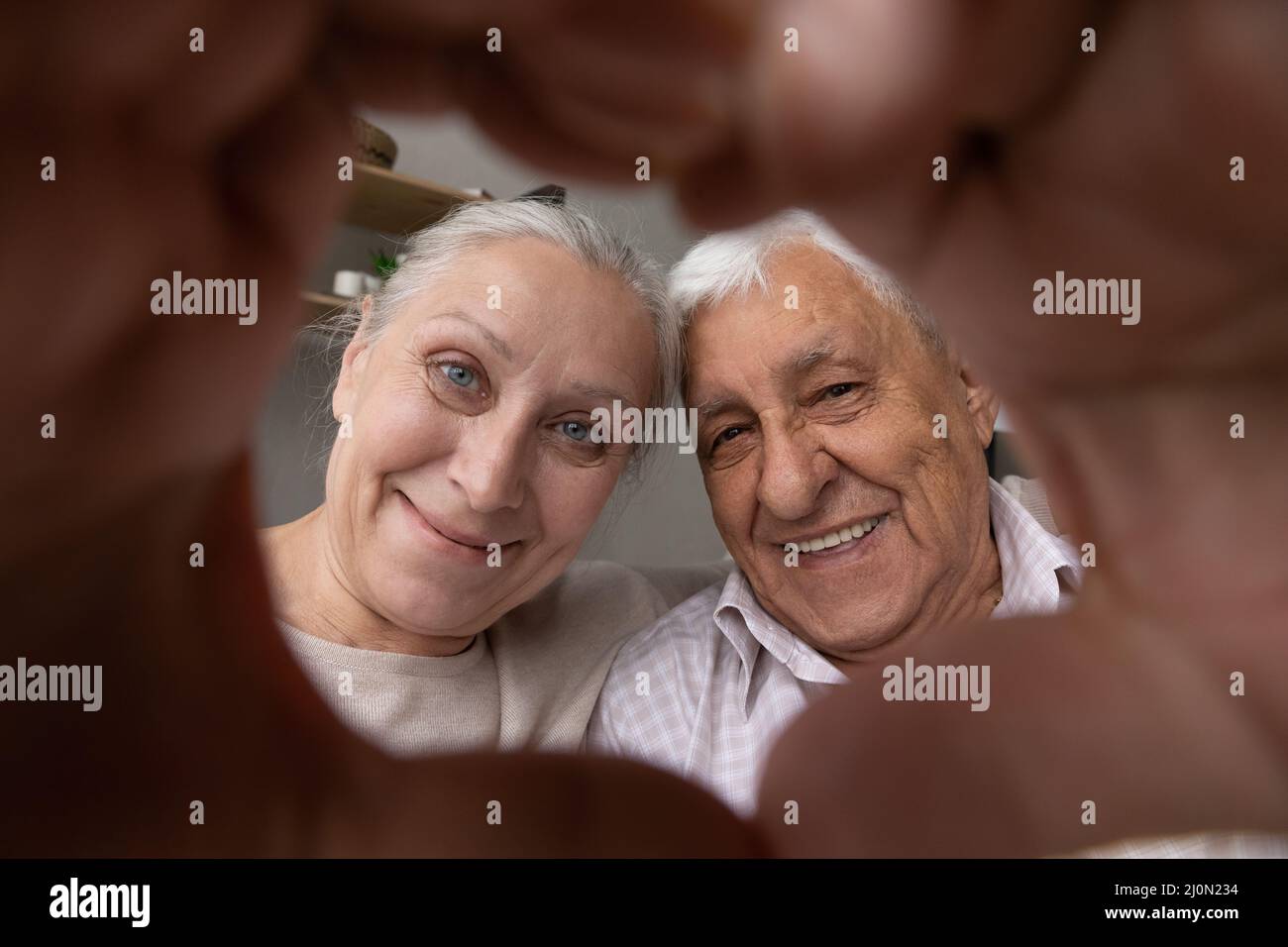 Coppia più anziana che guarda attraverso le loro dita unite che mostrano la forma del cuore Foto Stock