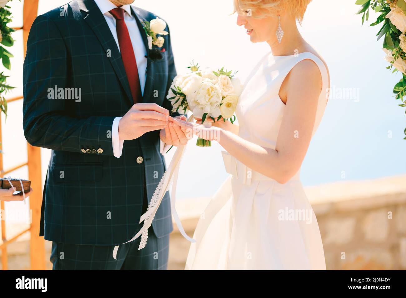 Sposi in un vestito nero plaid mette un anello di nozze sul dito per sposare in un abito bianco con un bouquet di fiori Foto Stock
