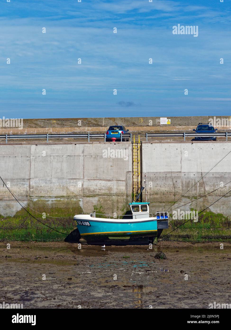 Una piccola barca da pesca costiera colorata che si posa sul limo a Low Tide, ormeggiata contro Seahouses Harbour Wall in una luminosa giornata di Summers nel mese di giugno. Foto Stock