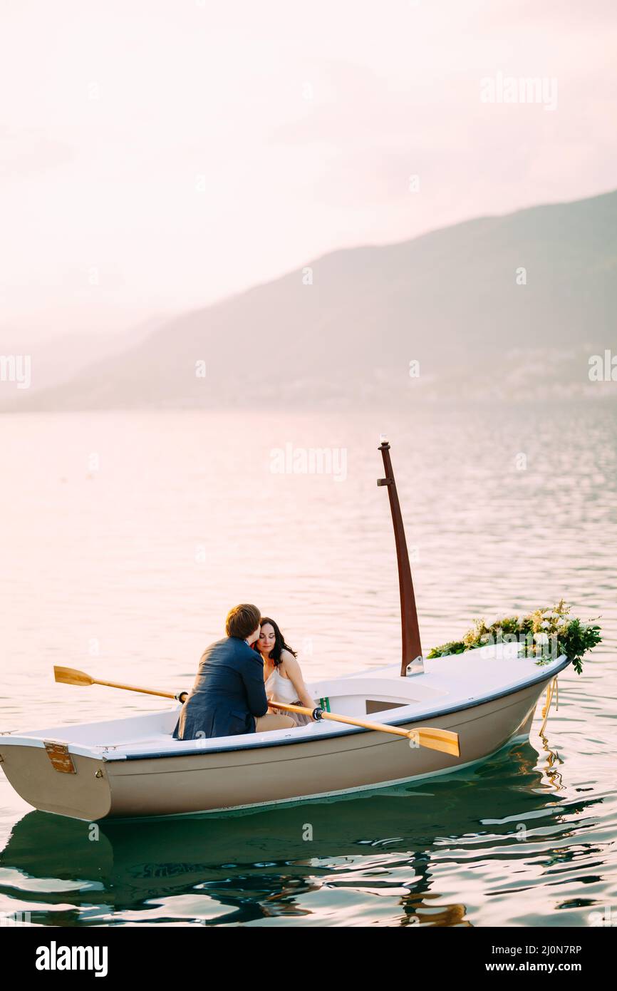 L'uomo bacia la donna sulla fronte in una barca decorata con fiori nel mezzo di un laghetto contro uno sfondo di montagne Foto Stock