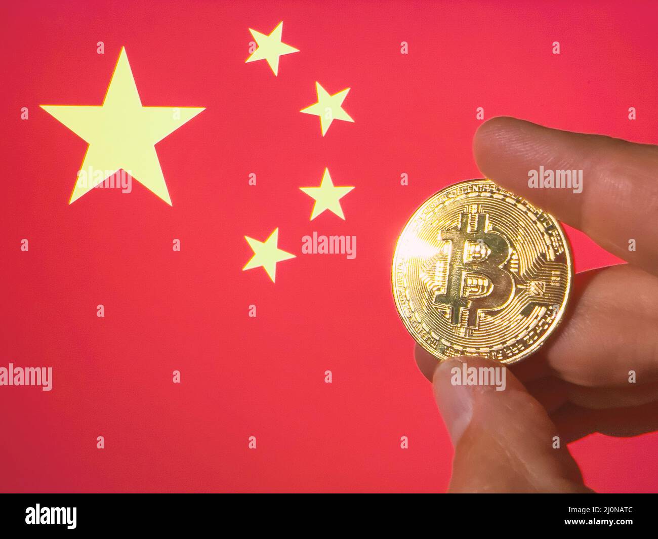 Tenere un Bitcoin fisico dorato sopra la bandiera cinese. La Cina come investitore in tecnologia di criptovaluta e blockchain. Contesto finanziario Foto Stock