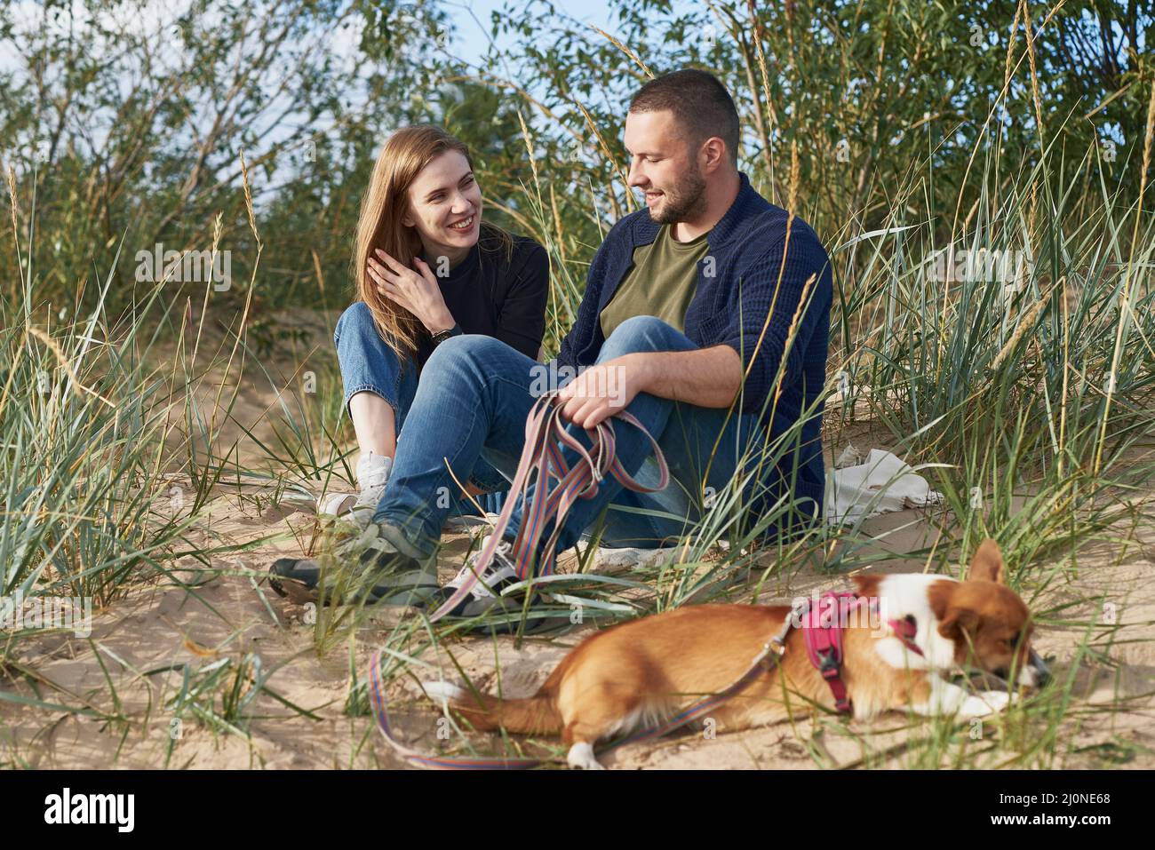 Giovane coppia felice con cane corgi che si trova sulla sabbia. Bell'uomo e bella donna Foto Stock