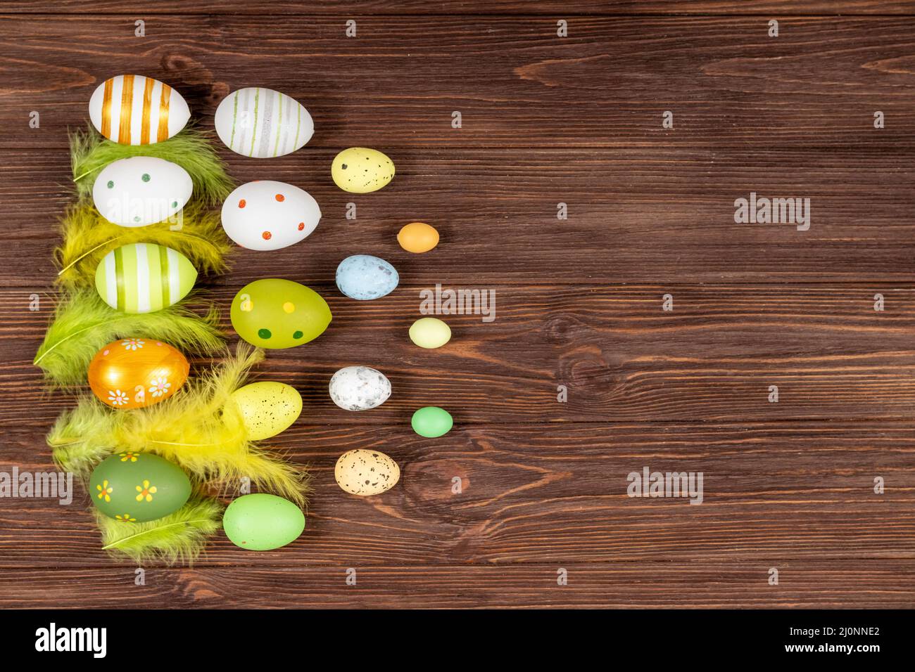 Felice Pasqua concetto. Uova di Pasqua colorate con piume luminose su sfondo di legno scuro. Vista dall'alto. Luogo per l'iscrizione, testo. Base per A. Foto Stock