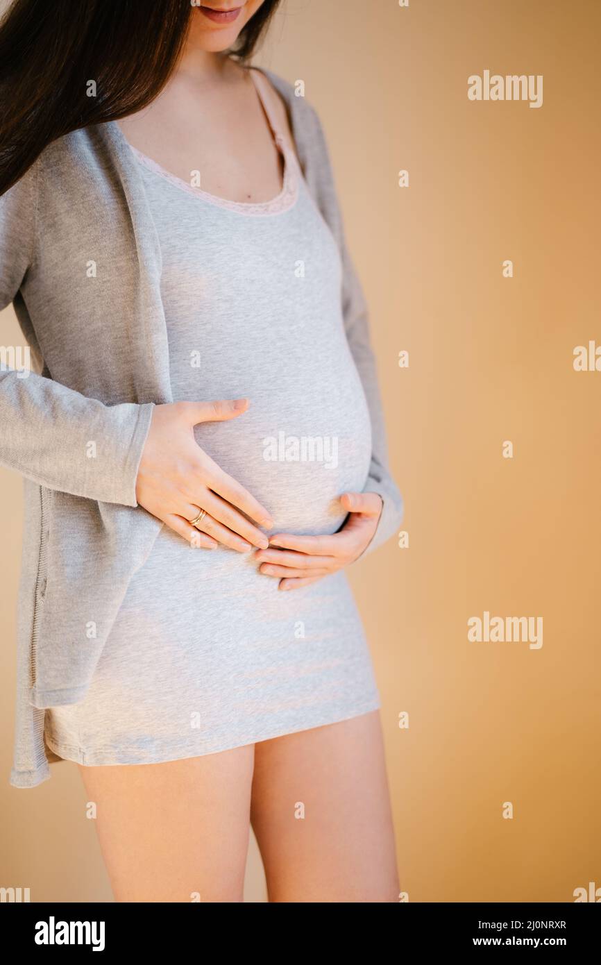 La donna incinta è in piedi accanto al muro che le tiene il pancino Foto Stock