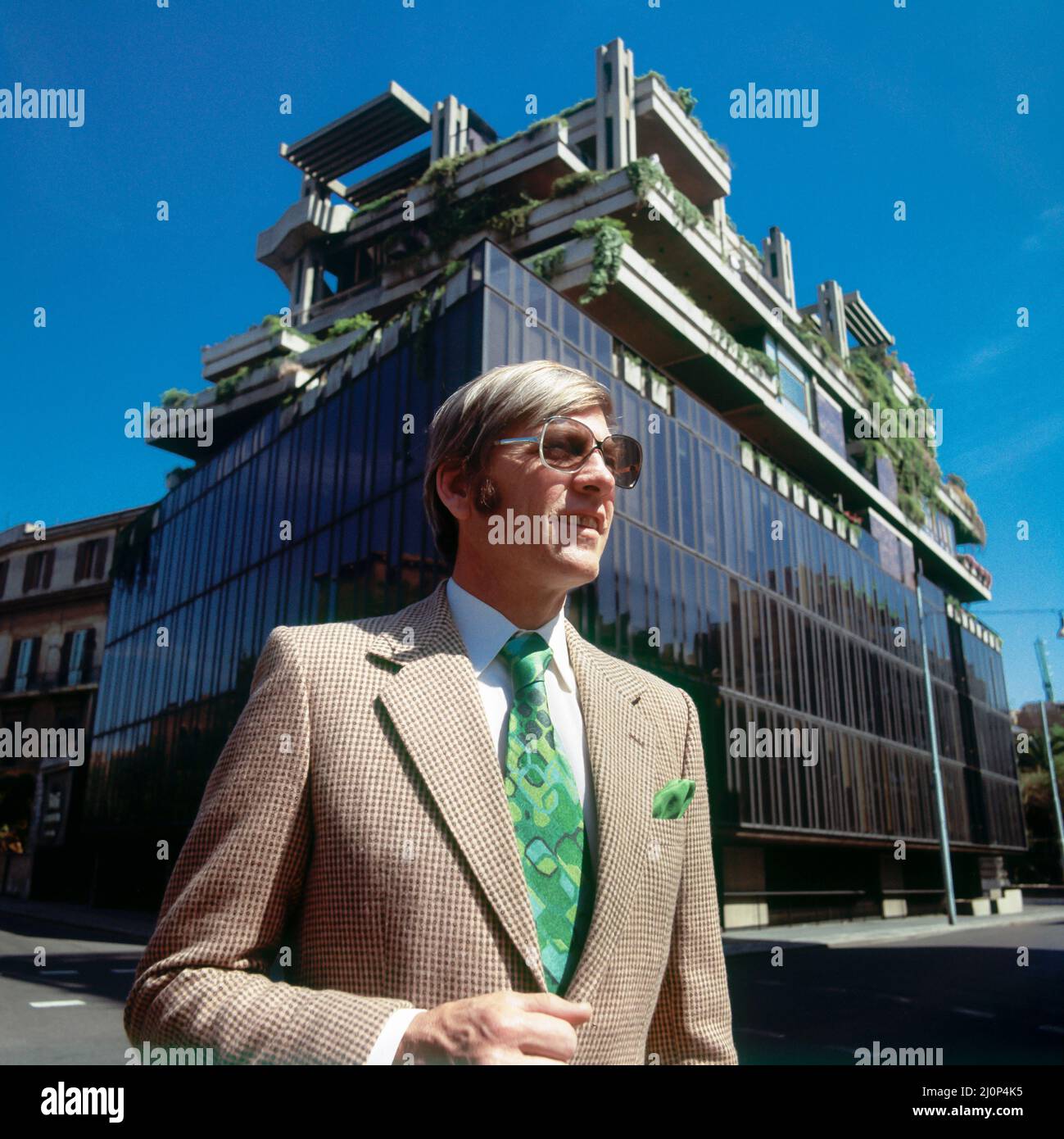 Vintage Rome 1970s, elegante ritratto uomo di mezza età con occhiali da sole di fronte ad un edificio moderno, Italia, Europa, Foto Stock