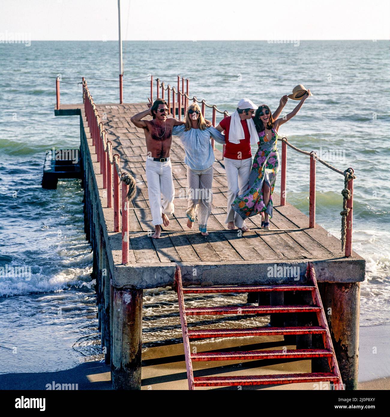 Vintage Italy 1970s, esuberante 2 coppie di amici gioiosi che corrono sul molo, Kursaal Beach, Lido di Ostia, Lazio, Europa, Foto Stock