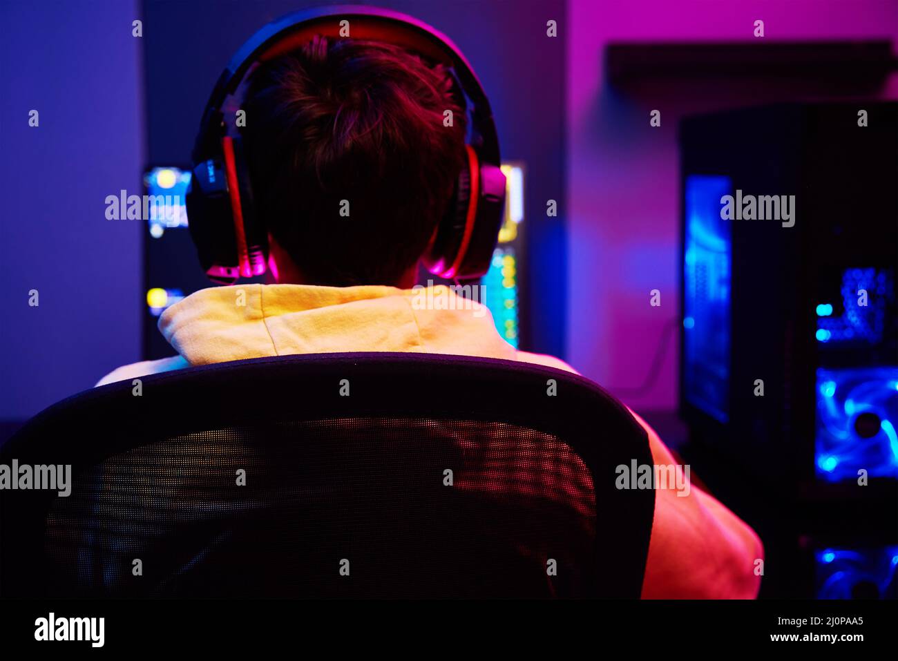Vista posteriore di ragazzo adolescente giocare video gioco computer in camera oscura, utilizzare neon colorato tastiera meccanica rgb, luogo per il gioco di cybersport Foto Stock