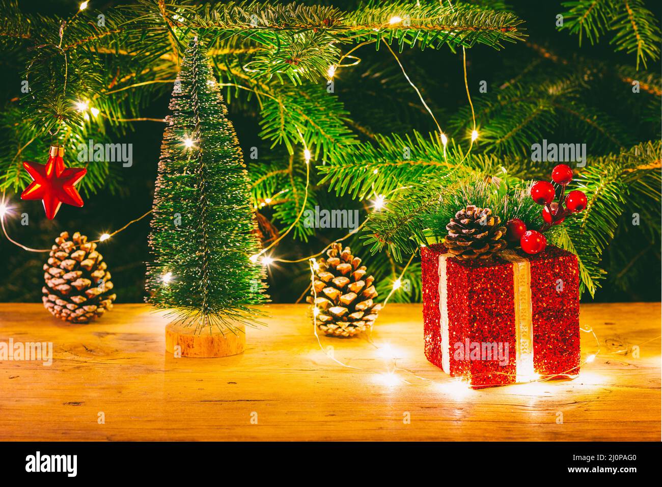 Una scatola rossa di Natale con un regalo, una stella rossa e un piccolo albero di Natale sullo sfondo di un abeto naturale con li di Natale Foto Stock