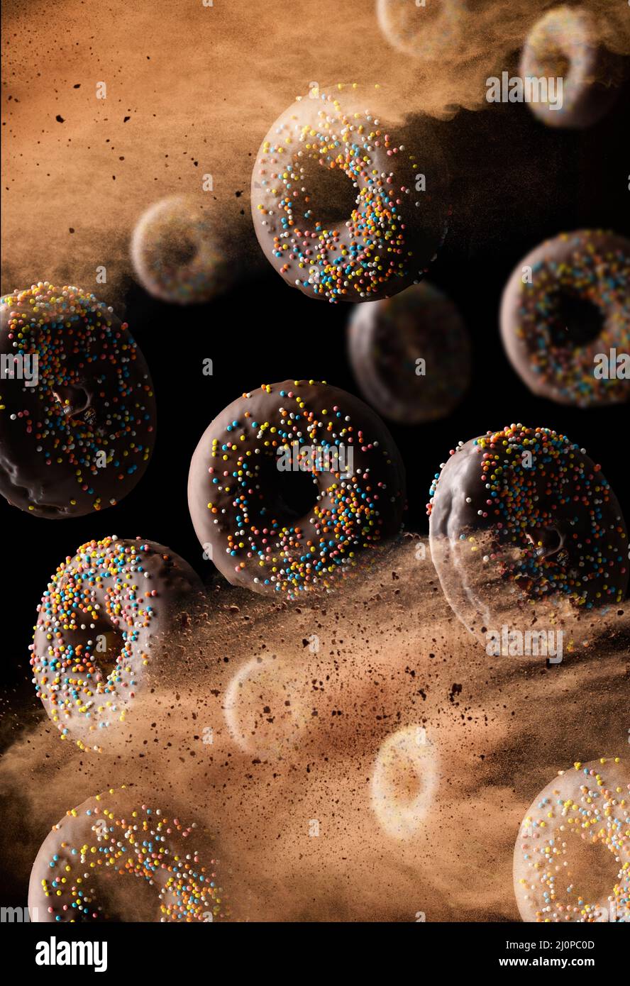 Ciambelle rotonde al cioccolato con zucchero multicolore cosparge di levitate in una nuvola di cacao marrone su sfondo nero. Polvere vola Foto Stock