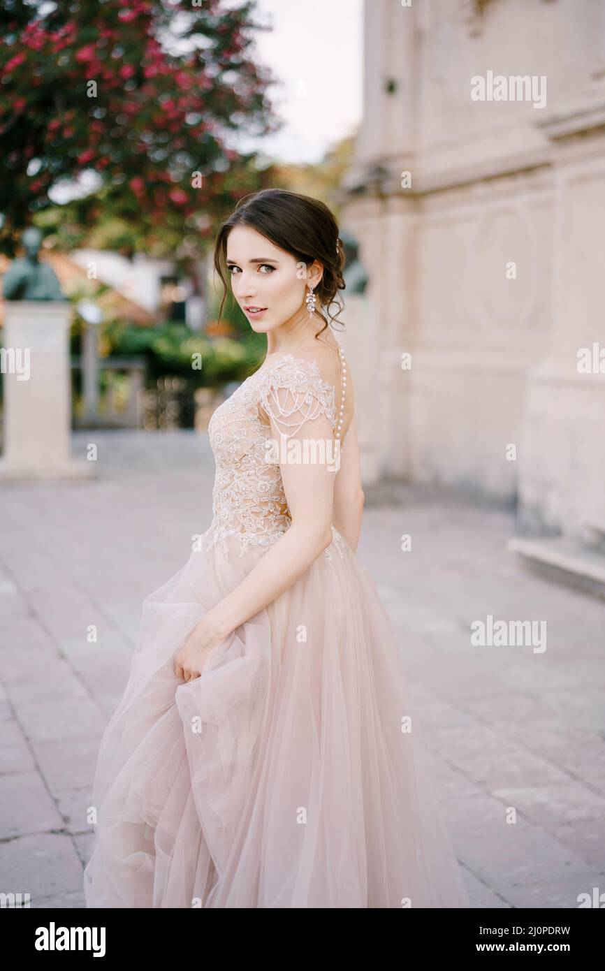 La sposa si trova vicino a un antico edificio che tiene con la mano l'orlo del suo vestito Foto Stock
