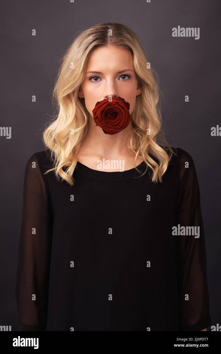 Silenziato dall'amore. Immagine concettuale di una donna bionda con una rosa che ricopre la bocca. Foto Stock